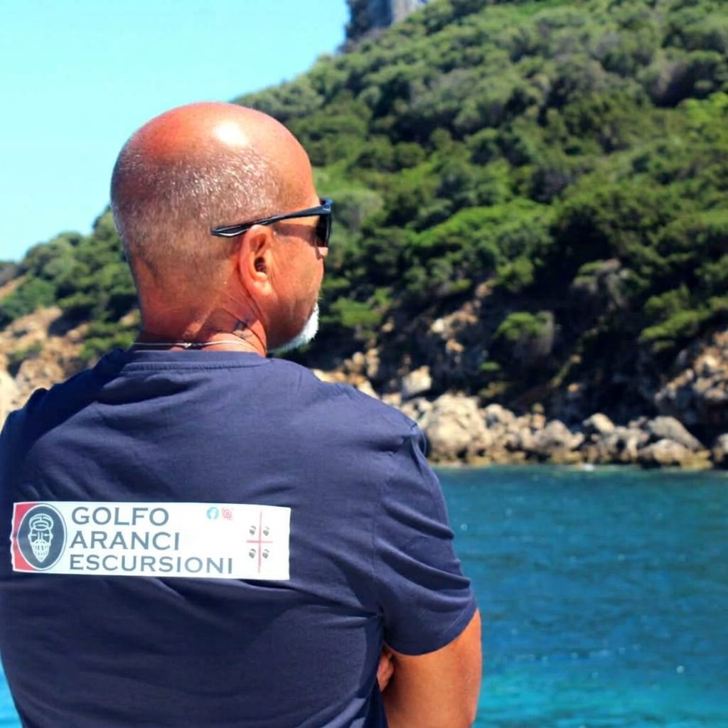 Uno degli skipper di Golfo Aranci Escursioni, di spalle, guarda la costa di Gallura dalla barca